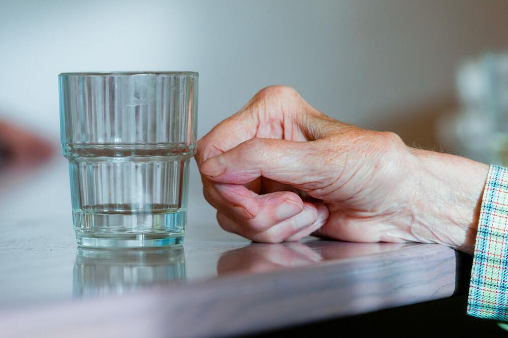 Eine ältere Hand am Wasserglas