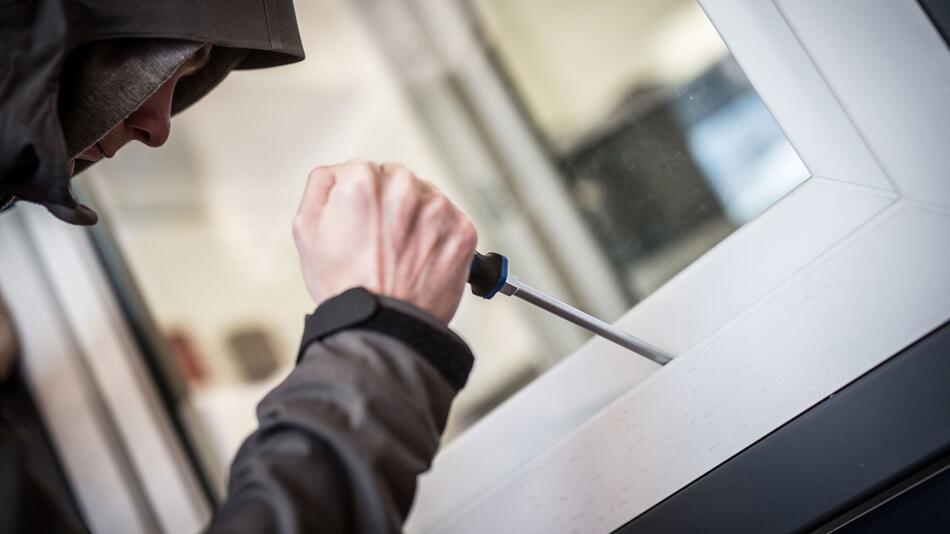 Ein Einbrecher hebelt mit einem Schraubendreher ein Fenster auf