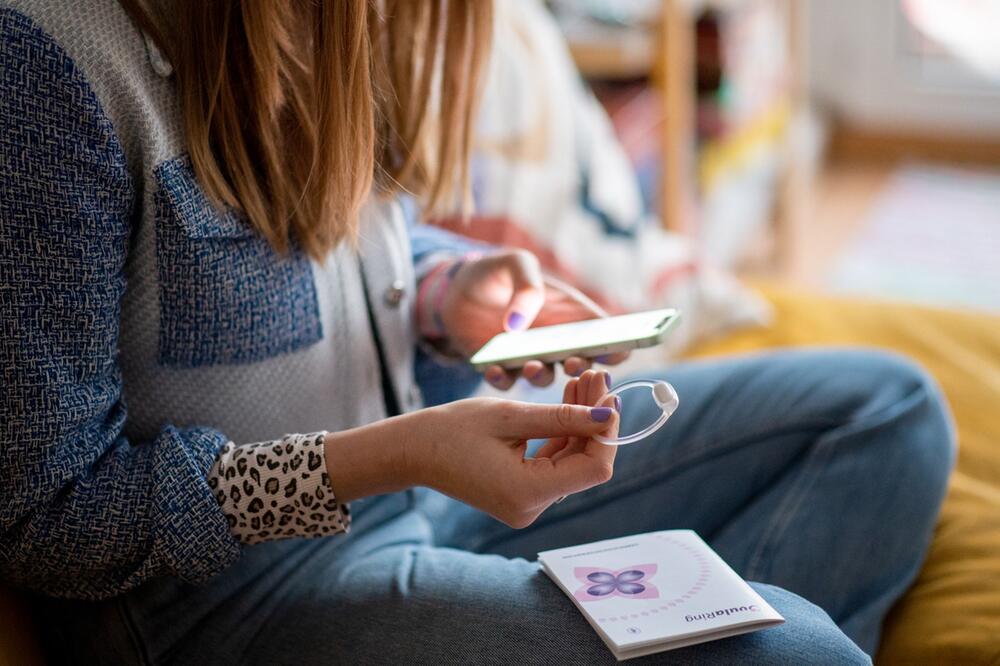 Eine Frau hält den Ovularing und ihr Smartphone in den Händen