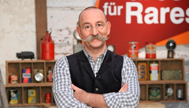 Horst Lichter vor einem Regal und dem "Bares für Rares"-Logo.