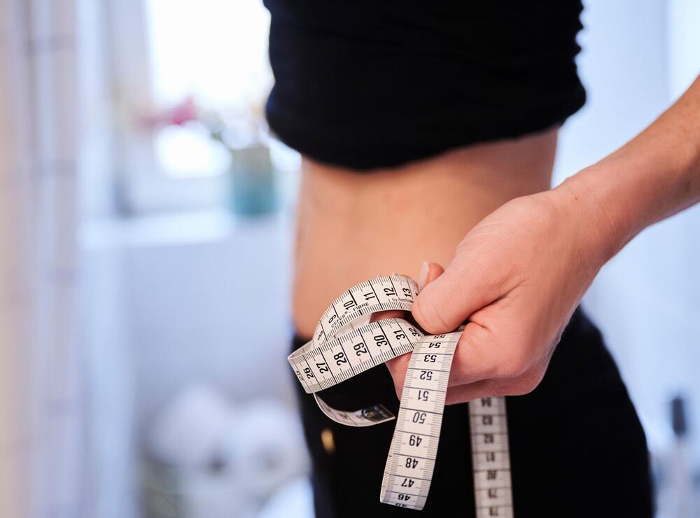 Eine junge Frau hält ein Zentimetermassband an ihren Bauch