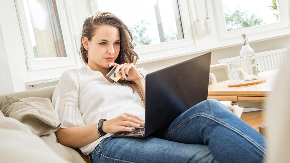 Frau mit Geldkarte in der Hand schaut auf einen Laptop