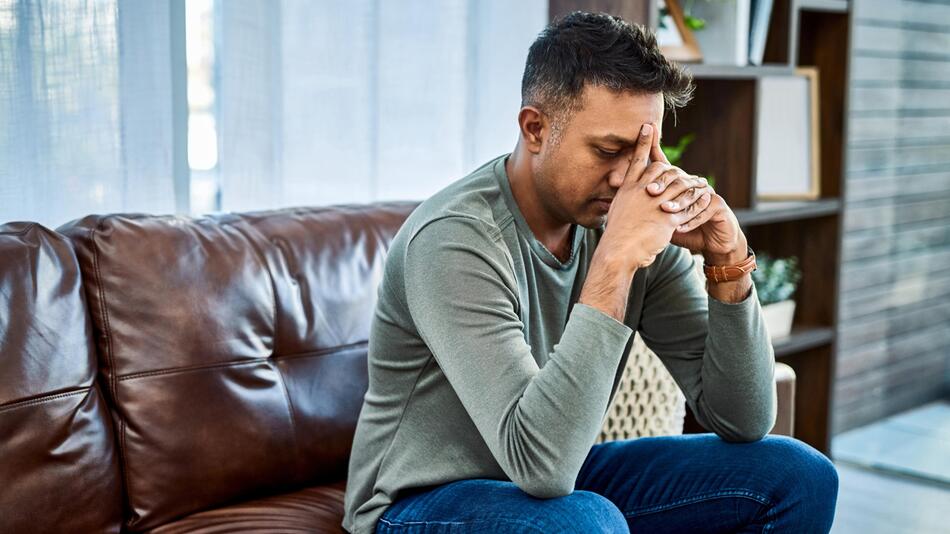 Mann sitzt auf dem Sofa und wirkt gestresst