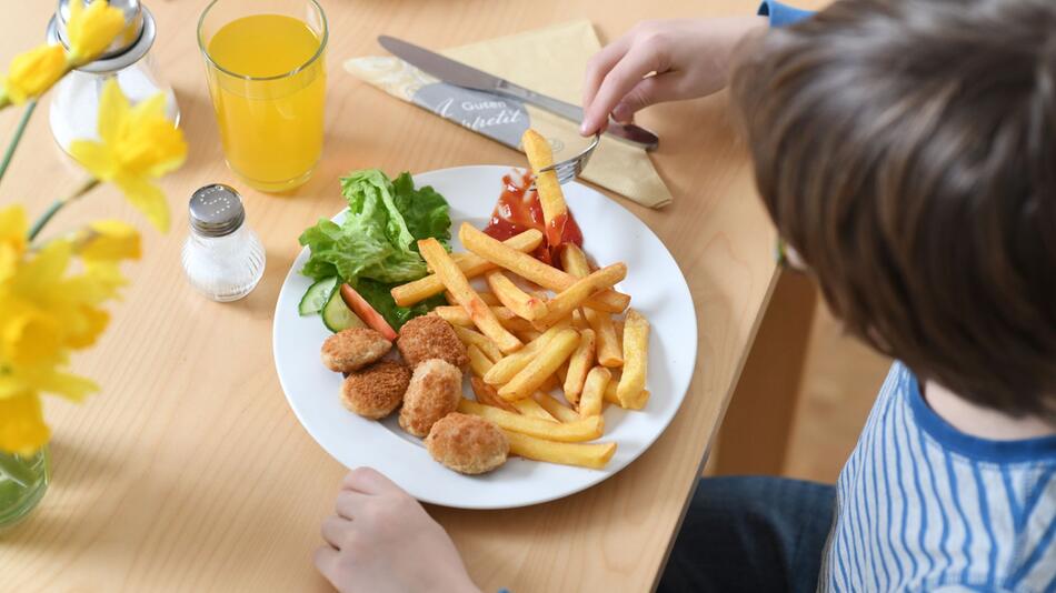 Kind isst Chicken Nuggets und Pommes Frites