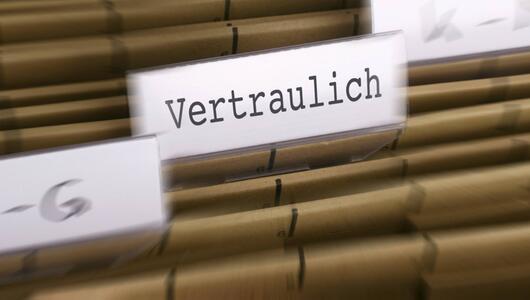 Braune Aktenordner mit Aufschriften auf Etiketten, ein Ordner mit der Aufschrift "Vertraulich"