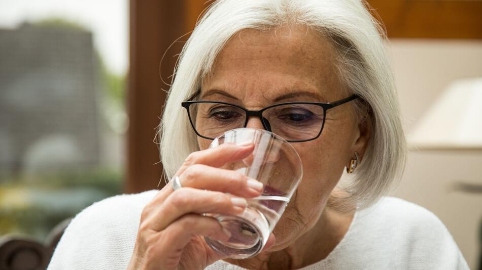 Eine Seniorin trinkt ein Glas Wasser
