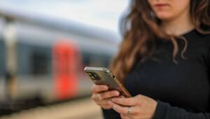 Eine junge Frau steht mit ihrem Mobiltelefon auf einem Bahnsteig