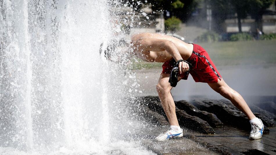 Ein Passant erfrischt sich bei grosser Hitze am Brunnen