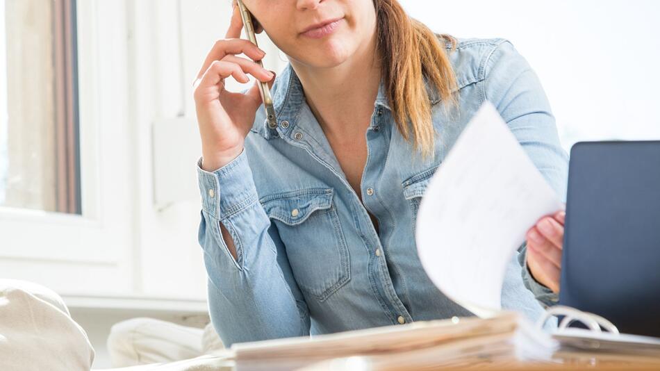 Eine Frau telefoniert und liest Unterlagen durch
