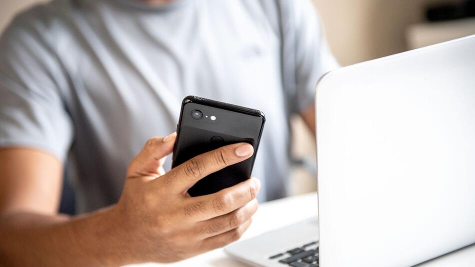 Junger Mann mit Smartphone und Laptop