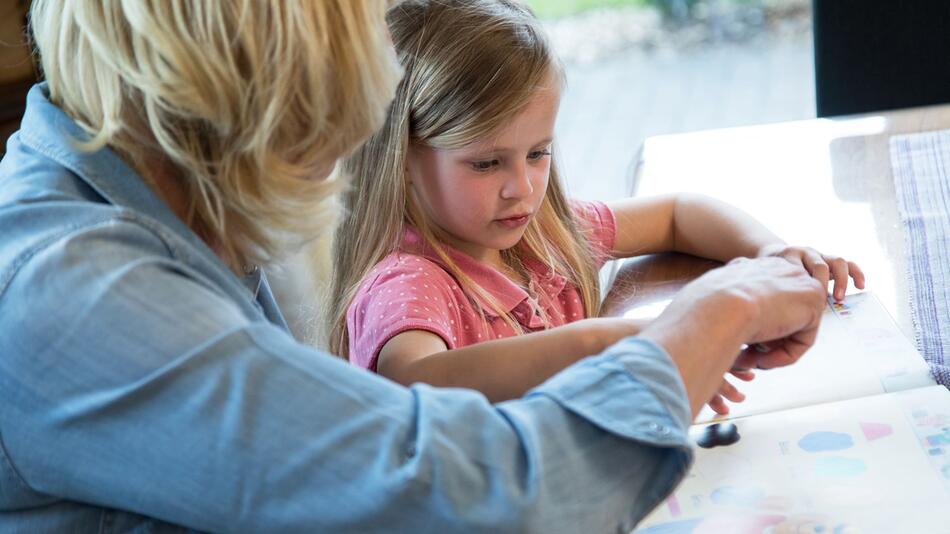 Frau schaut sich mit einem Mädchen ein Kinderbuch an