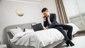 Ein Mann im Anzug sitzt auf einem Bett vor seinem Laptop