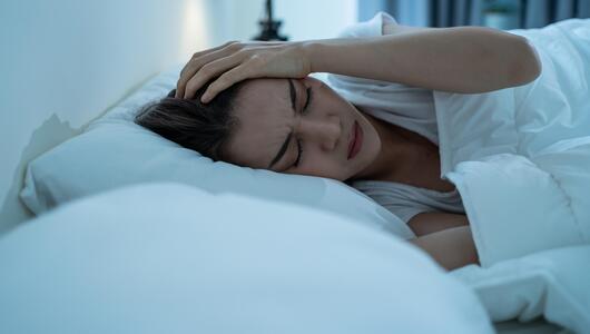 Frau liegt im Bett und hält sich den Kopf