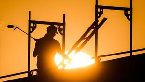 Ein Bauarbeiter im Gegenlicht der Sonne auf einem Gerüst