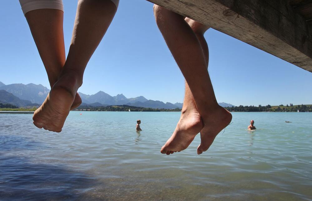 Badegäste lassen auf einem Steg am Forggensee Ihre Beine baumeln