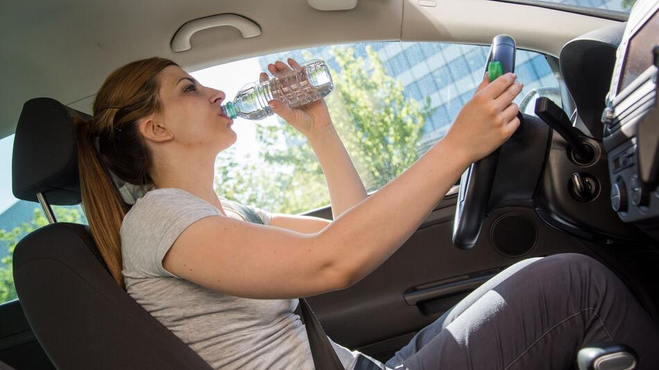Frau trinkt während der Autofahrt aus einer Wasserflasche