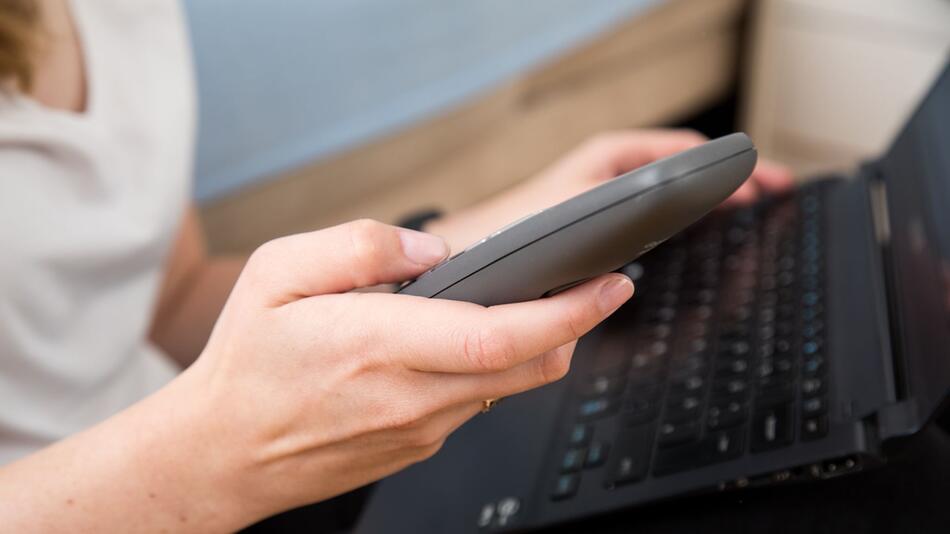 Eine Frau am Laptop wählt auf einem Telefon eine Nummer
