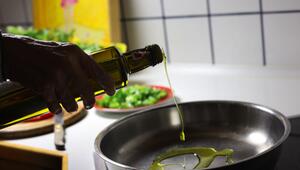 Frau gibt beim Kochen Olivenöl in eine Pfanne