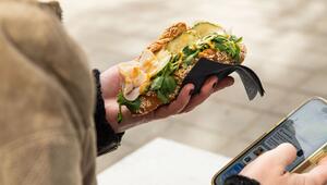 Eine Frau hält ein gefülltes Puten-Croissant und ihr Handy