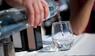 Mann giesst Wasser in ein Glas