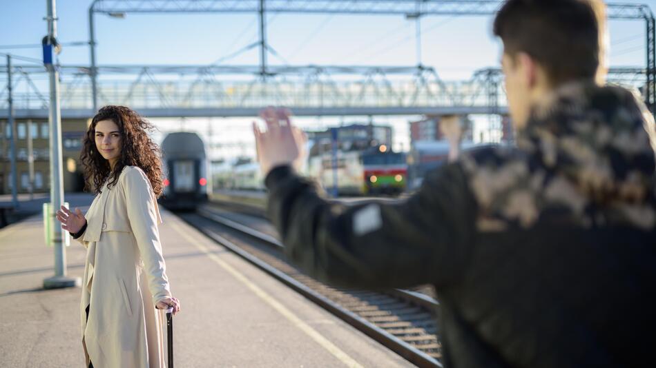 Ein Paar winkt sich am Bahngleis zum Abschied