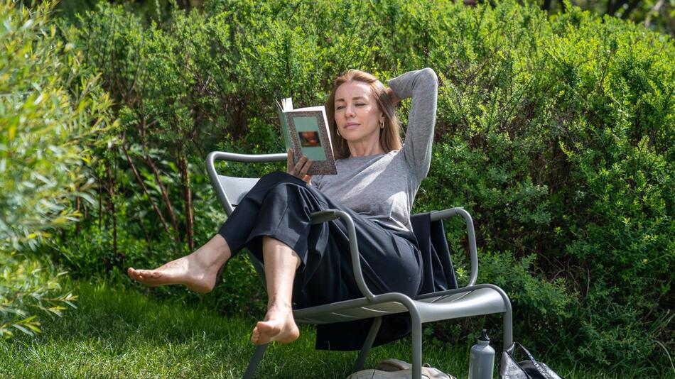 Eine Frau sitzt auf einem Gartenstuhl und liest ein Buch.