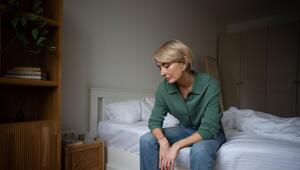 Eine Frau sitzt auf ihrem Bett und schaut bekümmert auf den Boden.