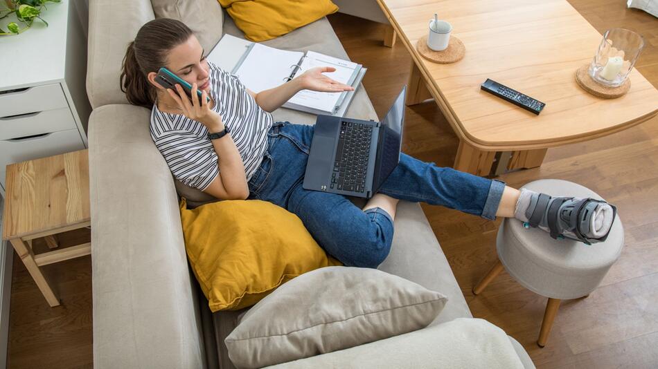 Eine Frau mit gebrochenen Fuss telefoniert auf dem Sofa