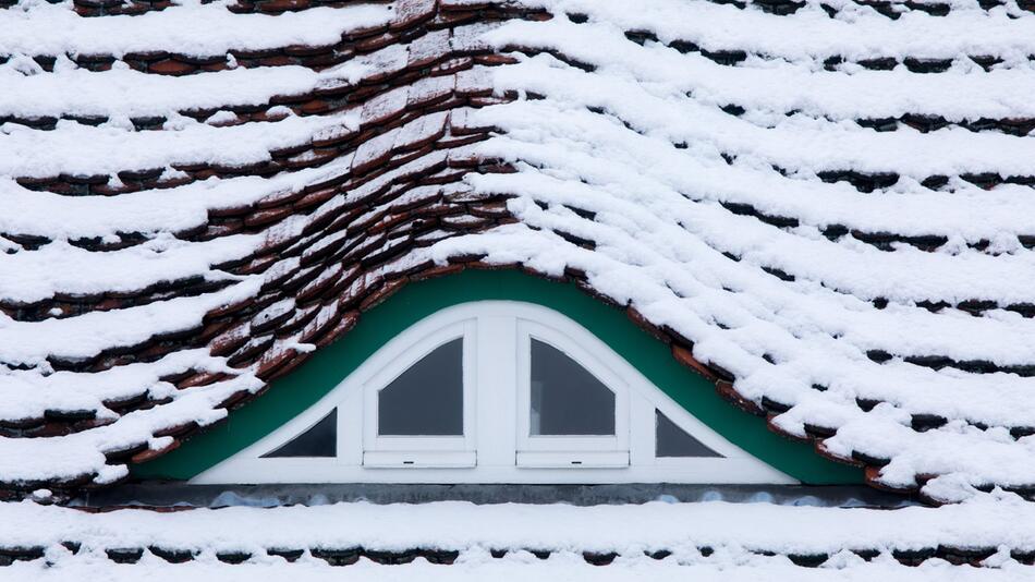 Schnee liegt auf einem Hausdach mit einer Fenstergaube