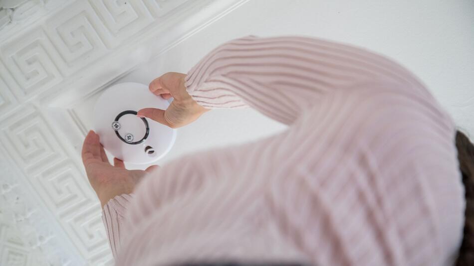 Eine Frau bringt einen Rauchmelder an