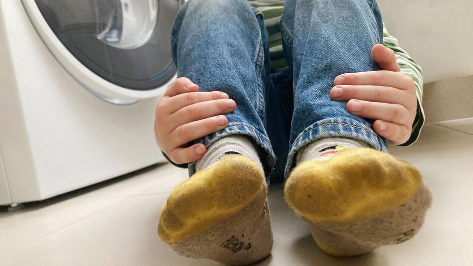 Kind mit schmutzigen Socken sitzt neben einer Waschmaschine